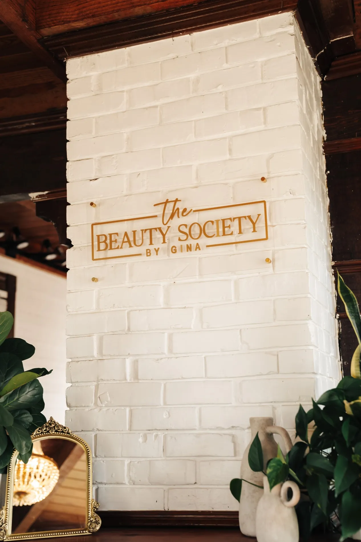 The Beauty Society by Gina signage on a whitewashed brick wall